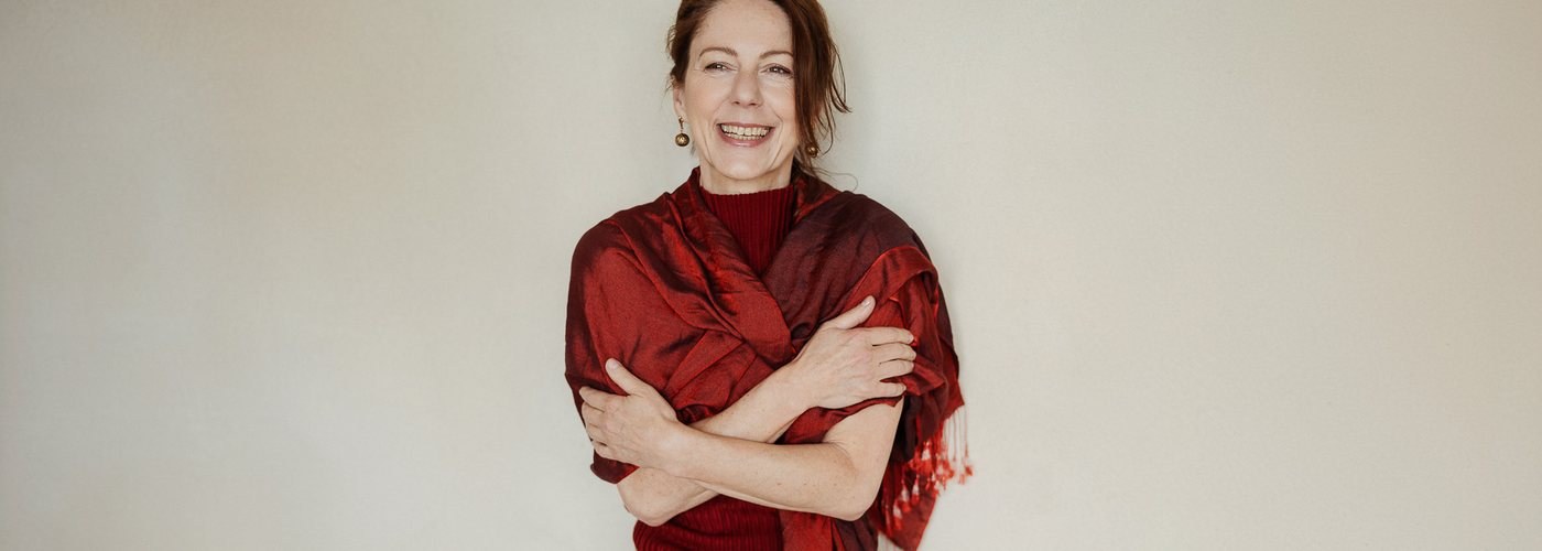Gabriella Rist im roten Tuch, die Arme vor der Brust verschränkt, lachend.