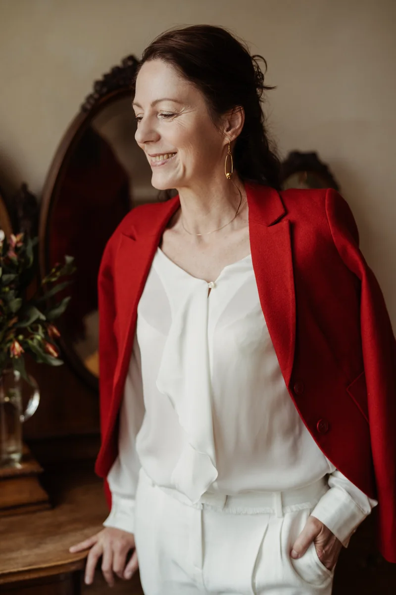 Gabriella Rist, Expertin für Entwicklungstrauma und Traumabegleitung, im roten Blazer und weißer Bluse, lächelnd zur Seite blickend
