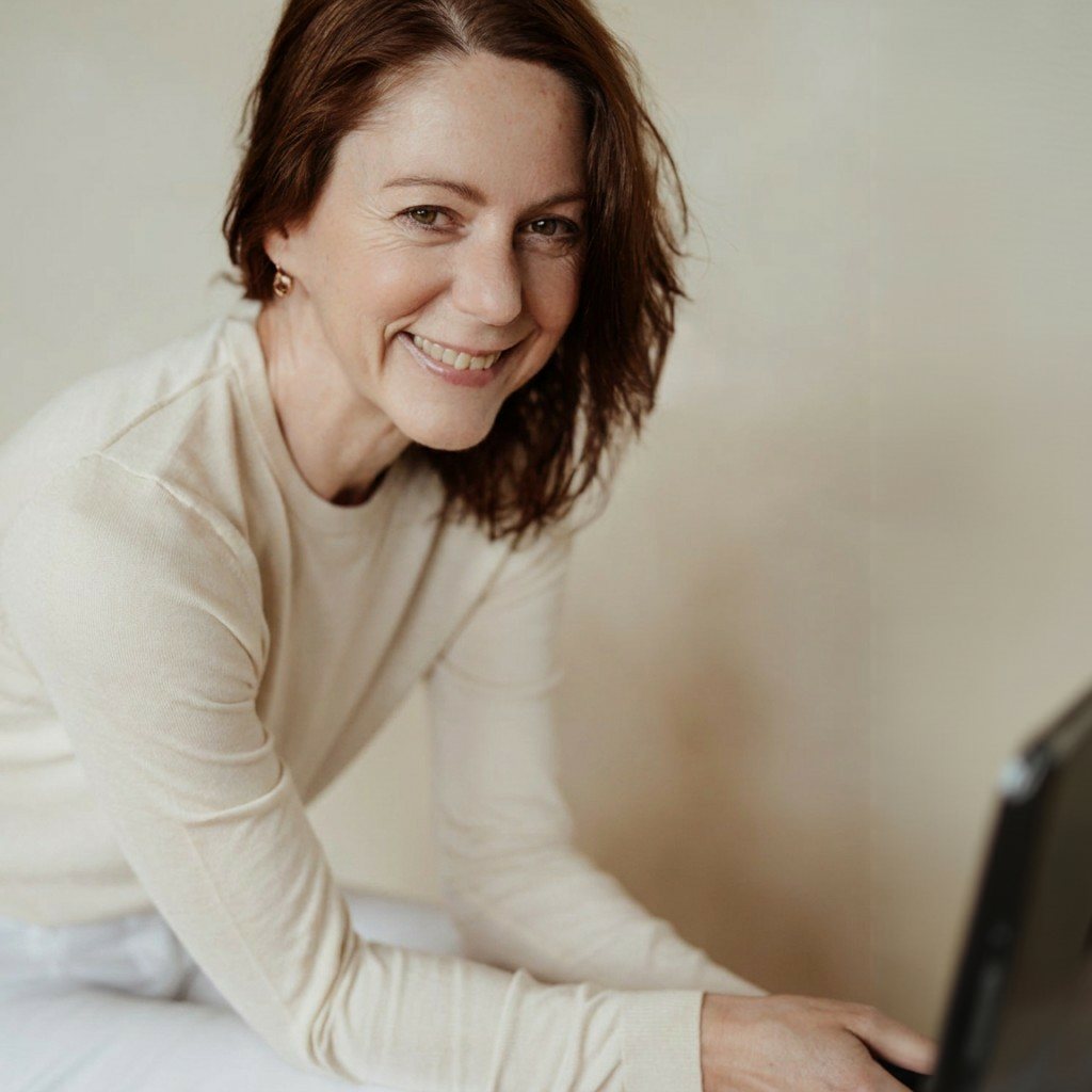 Gabriella Rist im hellen Oberteil am Laptop, lächelnd – Online Trauma Akademie: Module, Live-Klassen und Begleitung für das Nervensystem bei Entwicklungstrauma
