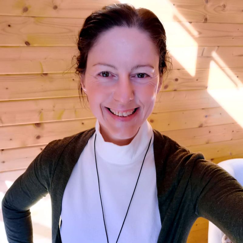 Gabriella Rist im weißen Oberteil, lächelnd, in einem hellen Holzraum – Expertin für Nervensystem und Entwicklungstrauma