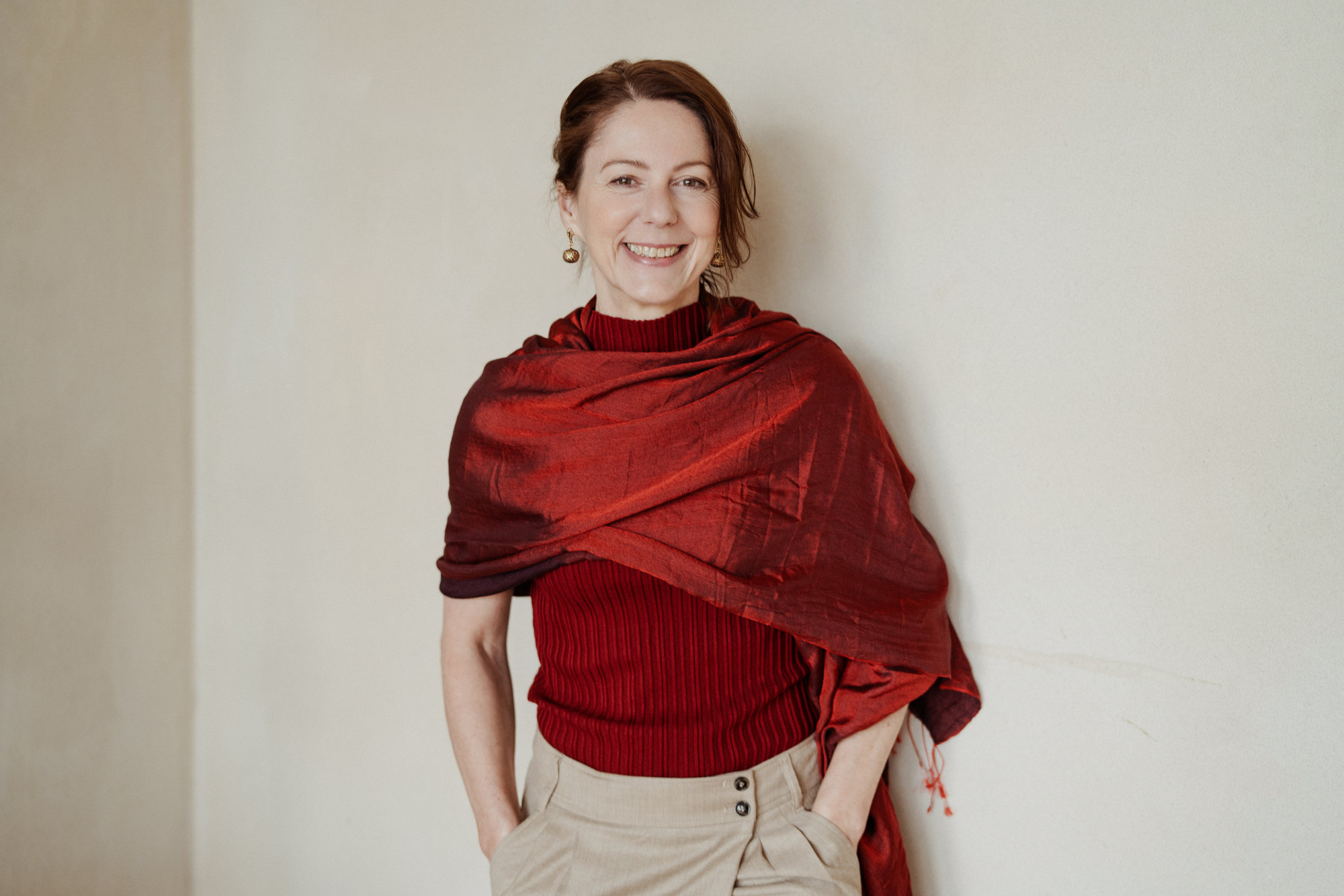 Gabriella Rist, Gründerin der GANESHASHALA® Trauma Fachakademie, im roten Tuch, die Arme um sich gelegt, lachend.