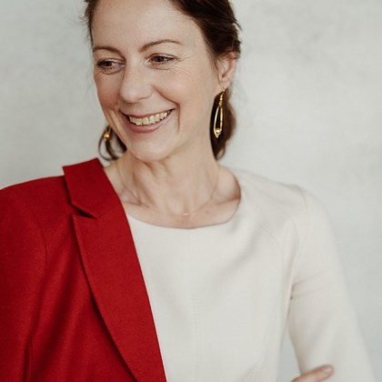 Porträt von Gabriella Rist, lachend, im roten Blazer.
